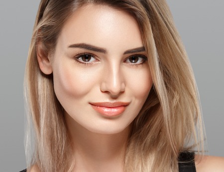 Beautiful young woman portrait smiling posing attractive blond with flying hair on gray background. Studio shot.の写真素材