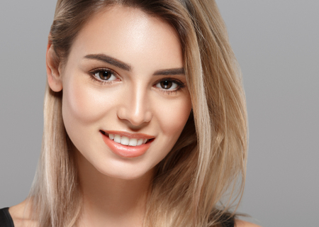 Beautiful young woman portrait smiling posing attractive blond with flying hair on gray background. Studio shot.の写真素材
