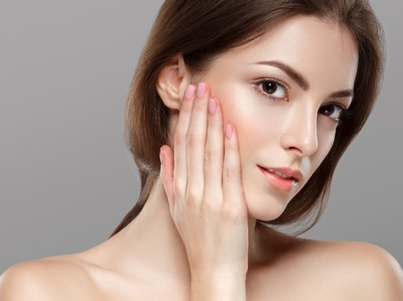 Young beautiful woman face portrait with healthy skin on gray background. Studio shot.