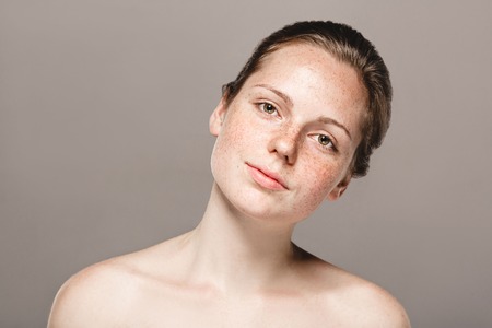 Young beautiful freckles woman face portrait with healthy skin. Studio shot. Isolated on gray.の写真素材