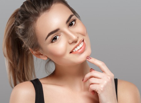 Beautiful young woman portrait smiling posing attractive blond with flying hair on gray background. Studio shot.の写真素材