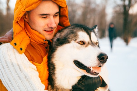 Man walking with dog winter time with snow in forest Malamute and Huskies friendship. Outdoor.