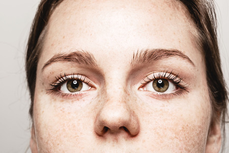 Eyes woman Young beautiful freckles woman face portrait with healthy skin. Gray background. Studio.の写真素材
