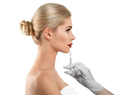 People, cosmetology, plastic surgery and beauty concept - beautiful young woman face and hand in glove with syringe making injectionの写真素材