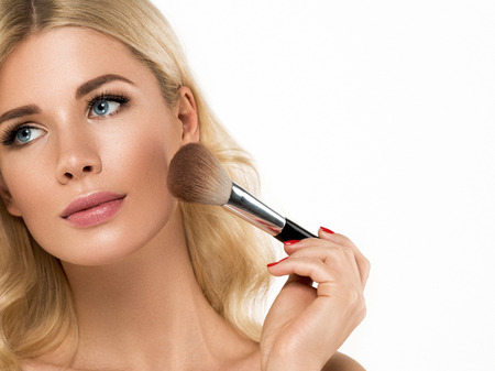 Young Beautiful Girl making makeup with brush on cheeks. Studio shot.の写真素材