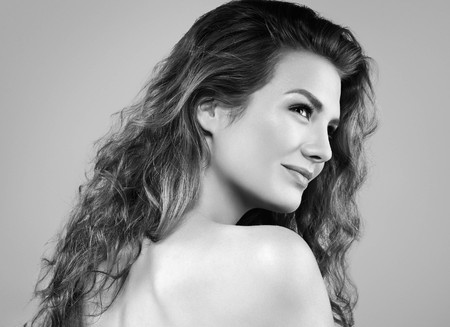 Beautiful woman face close up portrait young curly hair studio on gray. Black and white. Studio shotの写真素材
