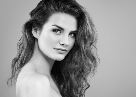 Beautiful woman face close up portrait young curly hair studio on gray. Black and white. Studio shotの写真素材