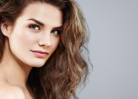 Beautiful woman face close up portrait young curly hair studio on gray.の写真素材