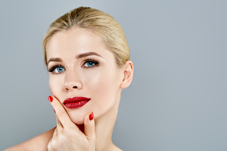 Beautiful Woman Blond face Portrait. Beautiful Spa model Girl with Perfect Fresh Clean Skin. Blonde female smiling. Youth and Skin Care Concept Red Lipstick and nails manicure.の写真素材