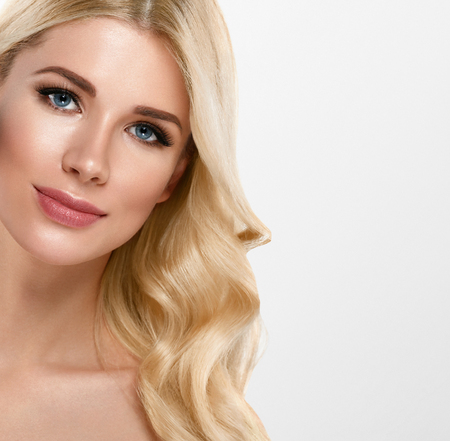 Beautiful Woman Portrait with fresh daily make-up blonde curly hair and healthy skin hands touching face skin. Studio shot.の写真素材