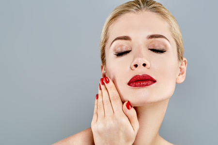 Beautiful Woman Blond face Portrait. Beautiful Spa model Girl with Perfect Fresh Clean Skin. Blonde female smiling. Youth and Skin Care Concept Red Lipstick and nails manicure.の写真素材