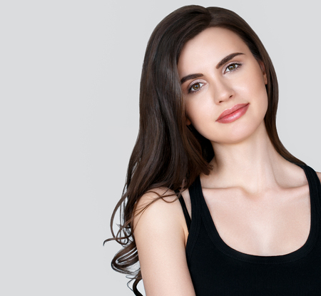 Beauty Woman face Portrait. Beautiful Spa model Girl with Perfect Fresh Clean Skin. Brunette female looking at camera and smiling on gray background. Beautiful hairstyle Youth and Skin Care Conceptの写真素材