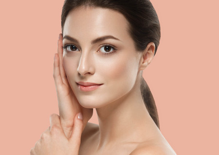 Beautiful Woman Girl brunette hair hands touching skin on summer pink trendy color background. Studio shot.の写真素材