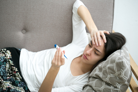 Young woman blowing nose in bed ill with temperature. Indoor shot.