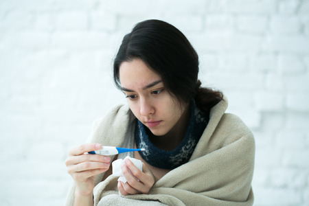 Young woman sick in bed with temperature drinks hot. Indoor shot.