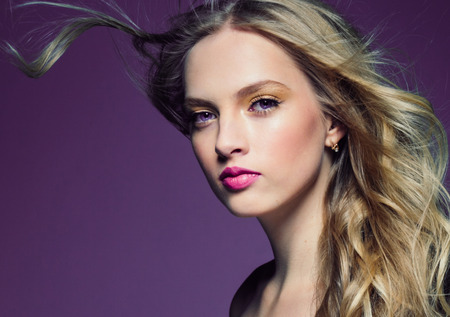 Beautiful blonde girl with long curly hair over purple background. Studio shot.の写真素材