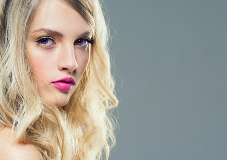 Beautiful blonde girl with long curly hair over purple background. Studio shot.の写真素材