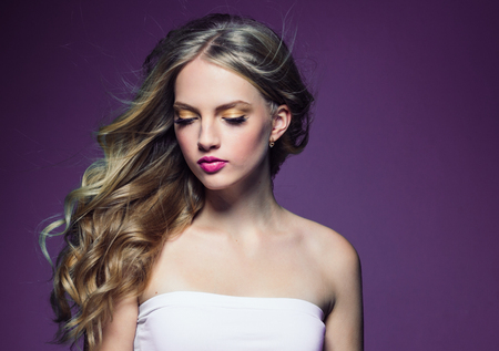 Beautiful blonde girl with long curly hair over purple background. Studio shot.の写真素材