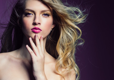 Beautiful blonde girl with long curly hair over purple background. Studio shot.の写真素材