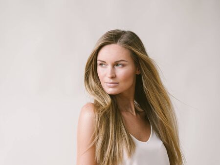 Beautiful woman natural portrait girl with long blonde hair over white gray wall. Studio shot.の写真素材
