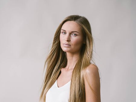 Beautiful woman natural portrait girl with long blonde hair over white gray wall. Studio shot.の写真素材