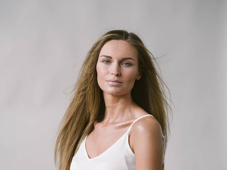 Beautiful woman natural portrait girl with long blonde hair over white gray wall. Studio shot.の写真素材