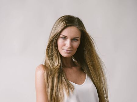 Beautiful woman natural portrait girl with long blonde hair over white gray wall. Studio shot.の写真素材