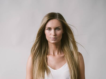 Beautiful woman natural portrait girl with long blonde hair over white gray wall. Studio shot.の写真素材
