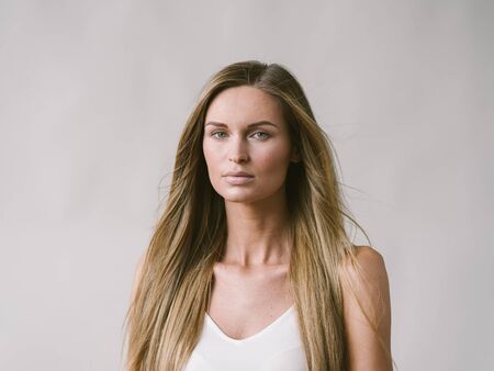 Beautiful woman natural portrait girl with long blonde hair over white gray wall. Studio shot.の写真素材