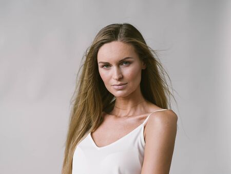 Beautiful woman natural portrait girl with long blonde hair over white gray wall. Studio shot.の写真素材