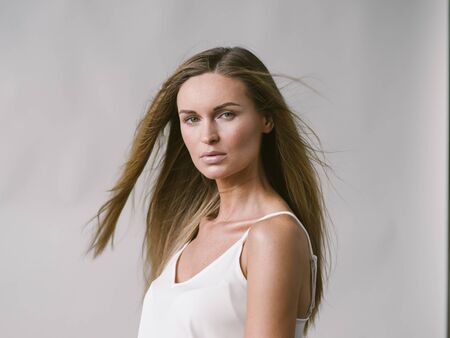 Beautiful woman natural portrait girl with long blonde hair over white gray wall. Studio shot.の写真素材