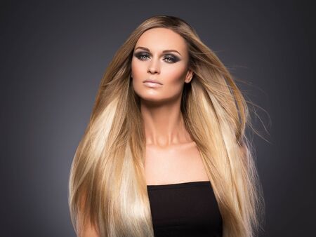 Hair beautiful long blond hairstyle woman fashion makeup healthy skin and hair black background. Studio shot.の写真素材