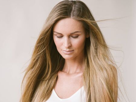 Beautiful woman natural portrait girl with long blonde hair over white gray wall. Studio shot.の写真素材