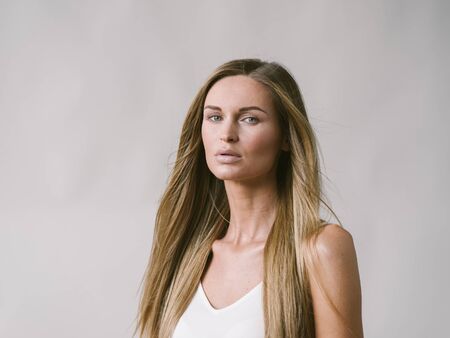 Beautiful woman natural portrait girl with long blonde hair over white gray wall. Studio shot.の写真素材