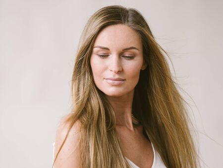 Beautiful woman natural portrait girl with long blonde hair over white gray wall. Studio shot.の写真素材