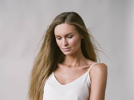 Beautiful woman natural portrait girl with long blonde hair over white gray wall. Studio shot.の写真素材