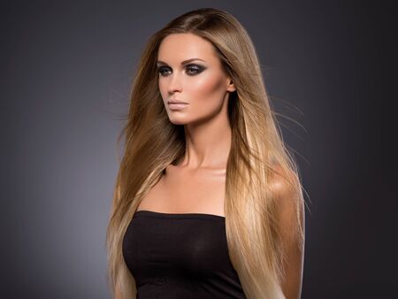 Hair beautiful long blond hairstyle woman fashion makeup healthy skin and hair black background. Studio shot.の写真素材