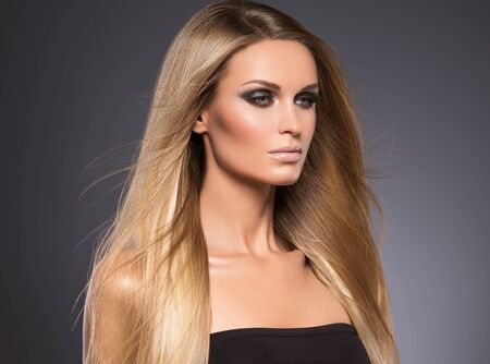 Hair beautiful long blond hairstyle woman fashion makeup healthy skin and hair black background. Studio shot.の写真素材