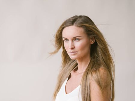 Beautiful woman natural portrait girl with long blonde hair over white gray wall. Studio shot.の写真素材