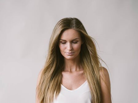 Beautiful woman natural portrait girl with long blonde hair over white gray wall. Studio shot.の写真素材