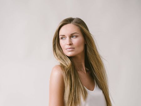 Beautiful woman natural portrait girl with long blonde hair over white gray wall. Studio shot.の写真素材