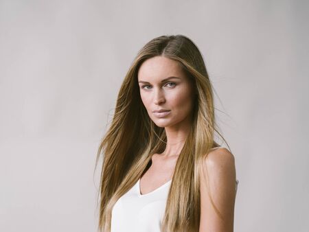 Beautiful woman natural portrait girl with long blonde hair over white gray wall. Studio shot.の写真素材