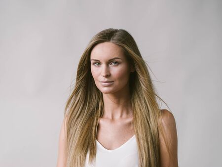 Beautiful woman natural portrait girl with long blonde hair over white gray wall. Studio shot.の写真素材