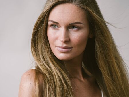 Beautiful woman natural portrait girl with long blonde hair over white gray wall. Studio shot.の写真素材