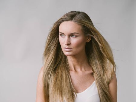 Beautiful woman natural portrait girl with long blonde hair over white gray wall. Studio shot.の写真素材