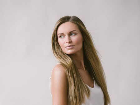 Beautiful woman natural portrait girl with long blonde hair over white gray wall. Studio shot.の写真素材