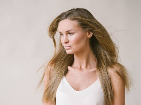 Beautiful woman natural portrait girl with long blonde hair over white gray wall. Studio shot.の写真素材