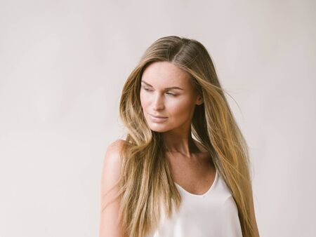 Beautiful woman natural portrait girl with long blonde hair over white gray wall. Studio shot.の写真素材