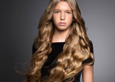 Long hair beauty girl healthy curly long hairstyle blonde in black dress. Studio shot.の写真素材