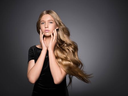 Long hair beauty girl healthy curly long hairstyle blonde in black dress. Studio shot.の写真素材
